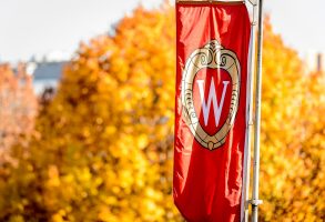An iconic W banner rustles in the wind on a colorful tree-lined sidewalk on Bascom Hill in fall at the University of Wisconsin-Madison on Nov. 4, 2016. (Photo by Bryce Richter / UW-Madison)